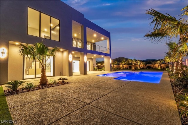 pool at dusk with a patio area and an outdoor pool