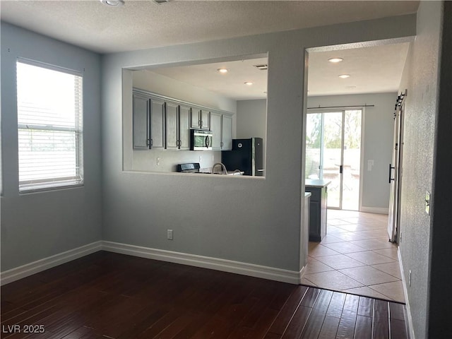 kitchen featuring baseboards, stainless steel microwave, hardwood / wood-style floors, freestanding refrigerator, and gray cabinets