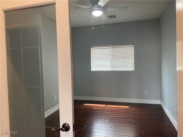 unfurnished room with a ceiling fan, visible vents, dark wood finished floors, and baseboards