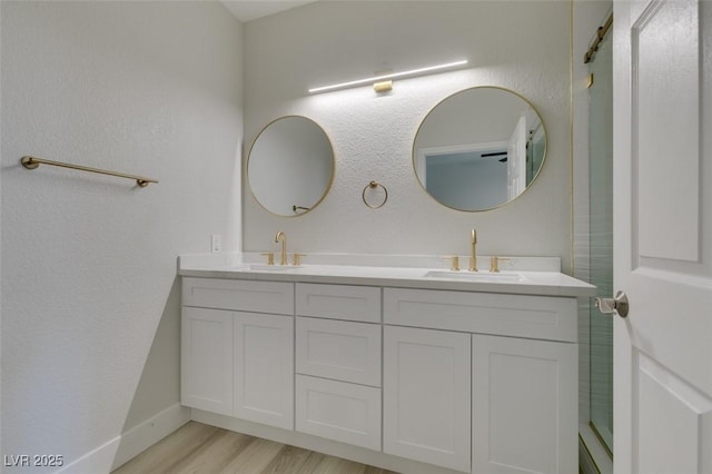 bathroom featuring double vanity, wood finished floors, a sink, and baseboards