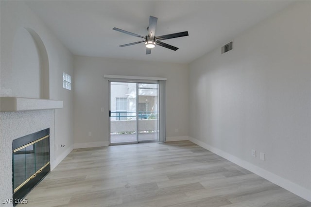 unfurnished living room featuring visible vents, a tiled fireplace, a ceiling fan, wood finished floors, and baseboards