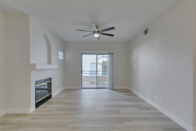 unfurnished living room with baseboards, visible vents, a ceiling fan, a tile fireplace, and light wood-style flooring