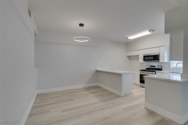 kitchen featuring a peninsula, a sink, white cabinetry, light countertops, and stainless steel range with gas stovetop