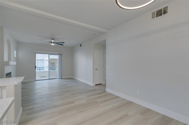 empty room with visible vents, a fireplace, light wood-style flooring, and baseboards