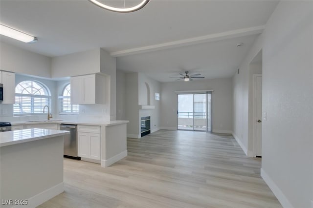 kitchen featuring a tile fireplace, light countertops, stainless steel appliances, white cabinetry, and a sink