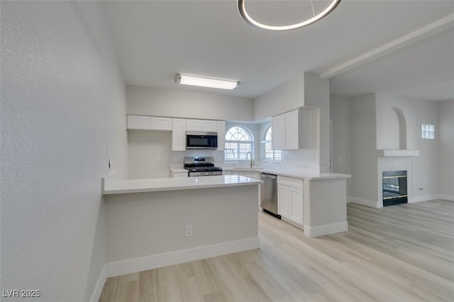 kitchen featuring stainless steel appliances, white cabinetry, a sink, and a peninsula