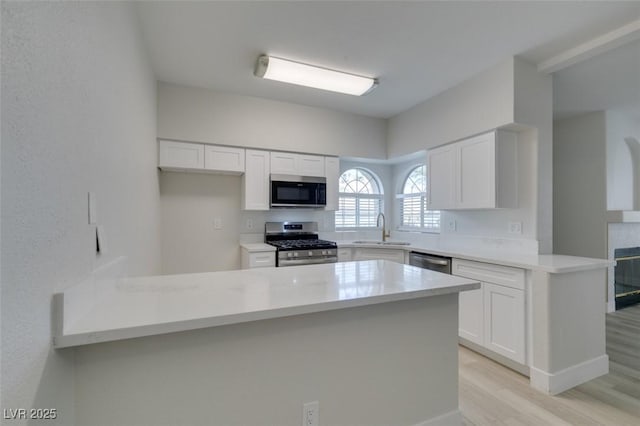 kitchen featuring appliances with stainless steel finishes, white cabinets, a sink, and a peninsula