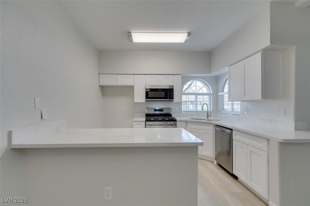 kitchen featuring appliances with stainless steel finishes, a peninsula, light wood-type flooring, white cabinetry, and a sink