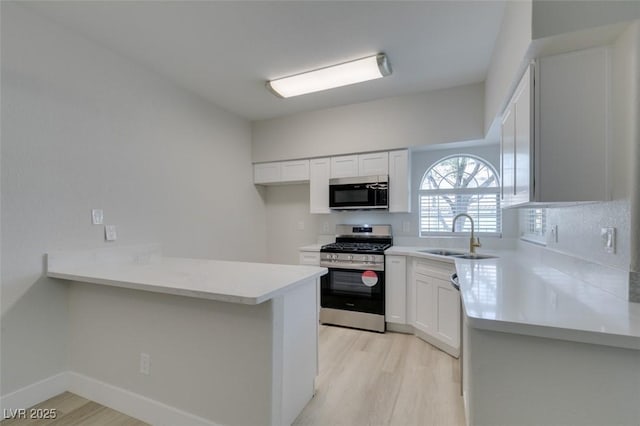 kitchen with light countertops, appliances with stainless steel finishes, a sink, and light wood-style floors