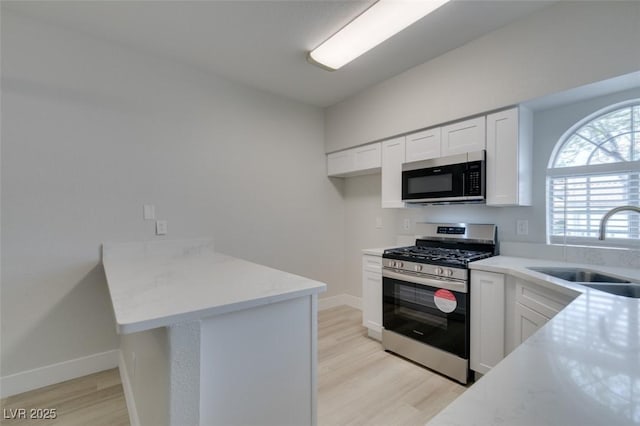 kitchen with light wood-style flooring, stainless steel appliances, a sink, white cabinetry, and light countertops