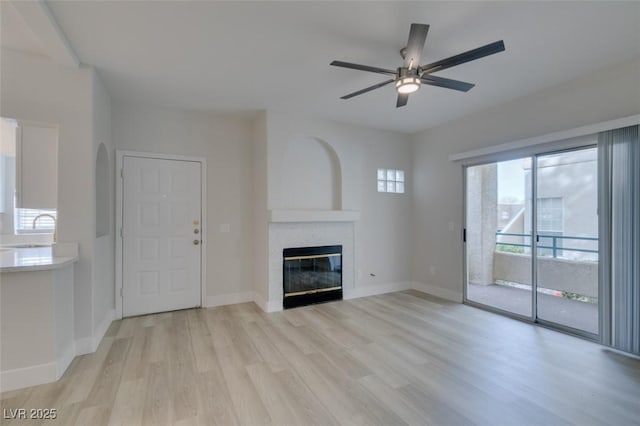 unfurnished living room featuring light wood-style floors, baseboards, ceiling fan, and a tiled fireplace