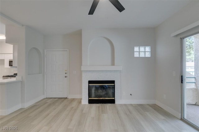 unfurnished living room featuring light wood-style floors, a fireplace, baseboards, and a ceiling fan