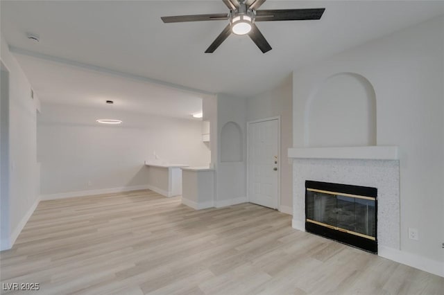 unfurnished living room with wood finished floors, a glass covered fireplace, a ceiling fan, and baseboards