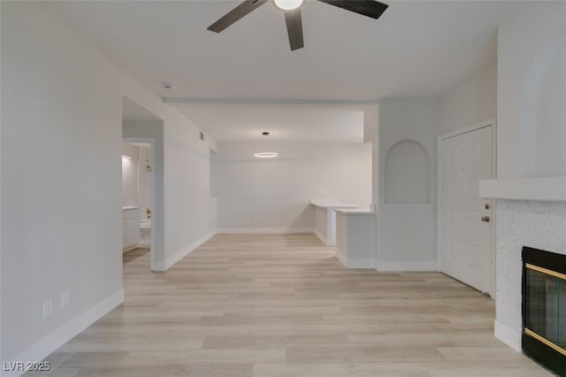 unfurnished living room featuring a glass covered fireplace, baseboards, ceiling fan, and light wood finished floors