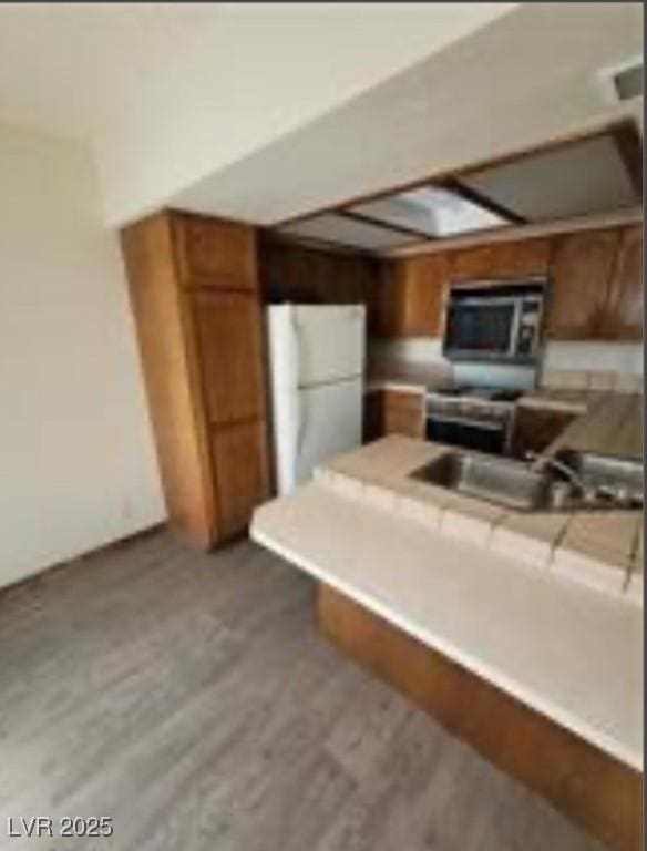 kitchen with stainless steel microwave, brown cabinets, freestanding refrigerator, a peninsula, and a sink