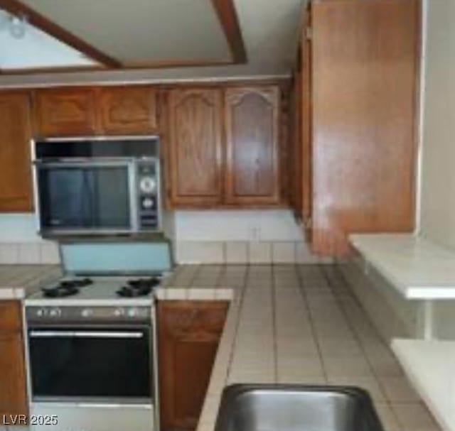 kitchen featuring stainless steel appliances, brown cabinetry, and light countertops