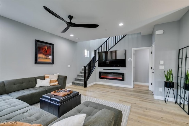 living area featuring recessed lighting, wood finished floors, baseboards, stairs, and a glass covered fireplace