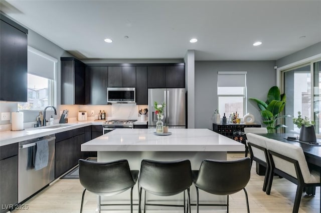 kitchen with a center island, a breakfast bar area, light wood-style flooring, appliances with stainless steel finishes, and a sink