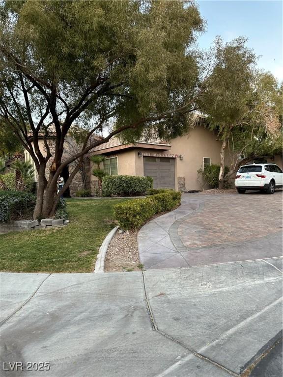 view of front of house with decorative driveway, a front yard, an attached garage, and stucco siding