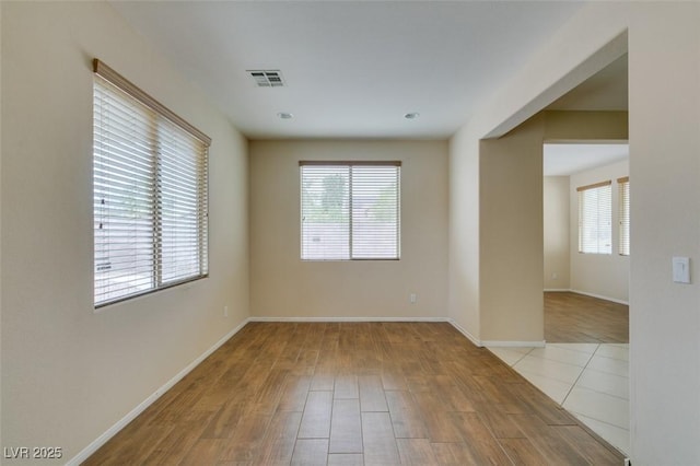 unfurnished room featuring a wealth of natural light, wood finished floors, visible vents, and baseboards