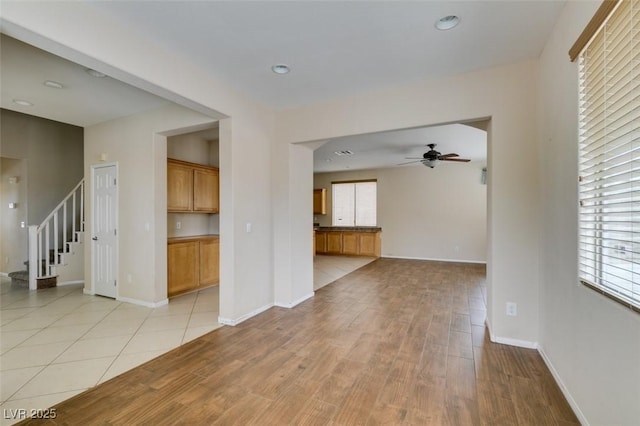 unfurnished living room featuring plenty of natural light, light wood finished floors, ceiling fan, and stairway