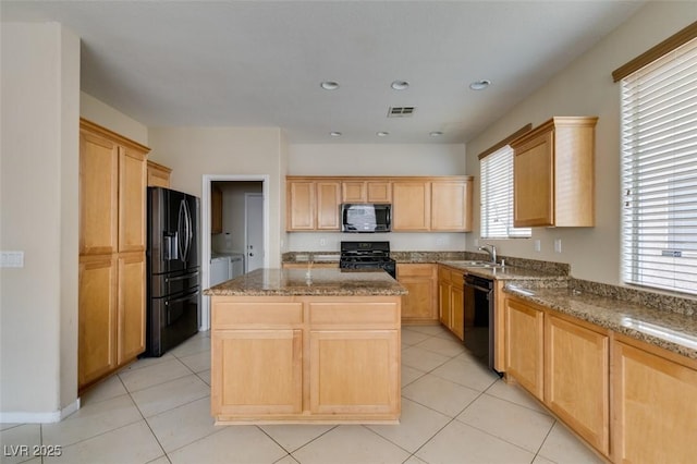 kitchen featuring light stone counters, a kitchen island, black appliances, and light brown cabinetry