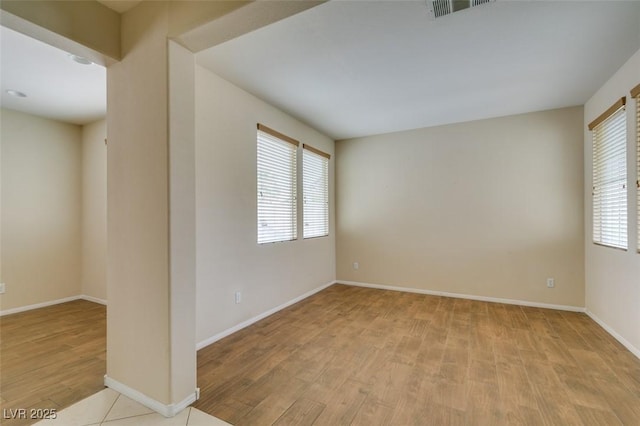 unfurnished room with baseboards, visible vents, a wealth of natural light, and wood finished floors