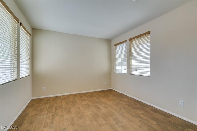 empty room with wood finished floors, a wealth of natural light, and baseboards