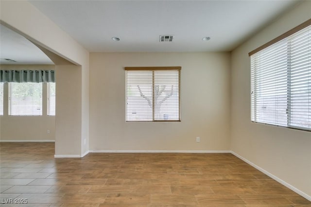 spare room with light wood-style floors, arched walkways, visible vents, and baseboards