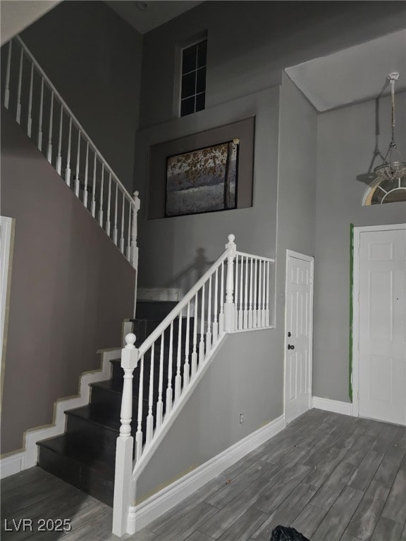 stairway featuring baseboards, a high ceiling, and wood finished floors