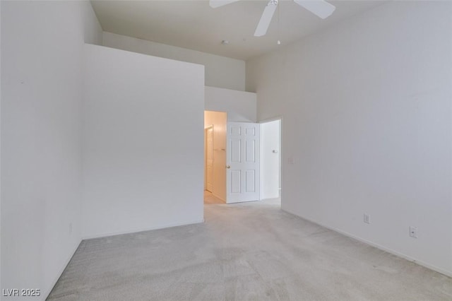 spare room with a ceiling fan, light colored carpet, and a towering ceiling