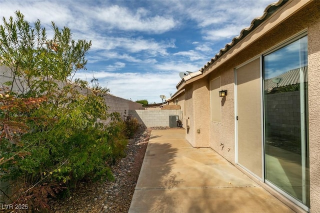 view of side of home featuring a patio, central AC unit, a fenced backyard, a tile roof, and stucco siding