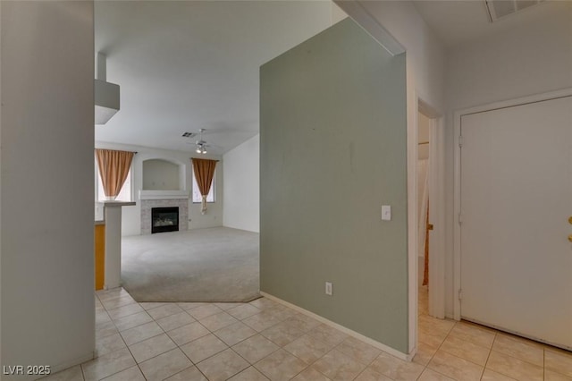 unfurnished living room with light tile patterned floors, visible vents, light colored carpet, a ceiling fan, and a tile fireplace