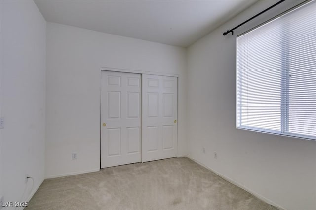 unfurnished bedroom featuring light carpet, a closet, and baseboards