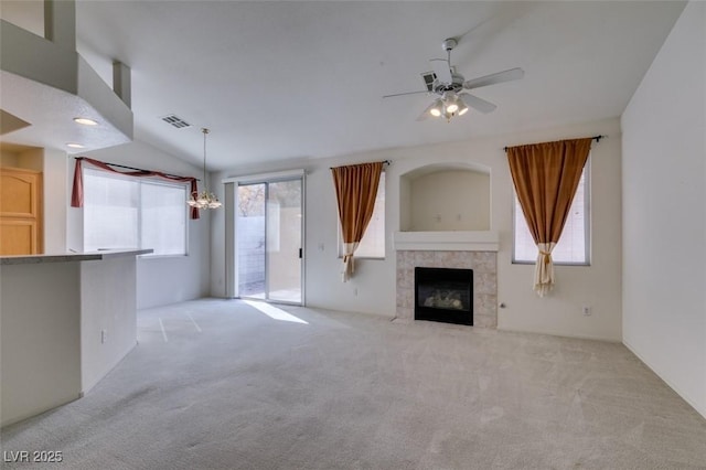 unfurnished living room with ceiling fan with notable chandelier, visible vents, a tiled fireplace, and light colored carpet