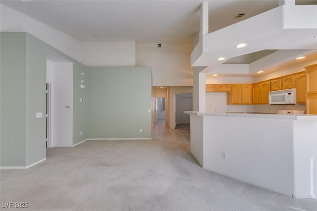 kitchen featuring visible vents, light colored carpet, white microwave, a high ceiling, and recessed lighting