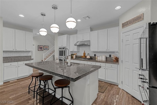 kitchen featuring under cabinet range hood, wood finished floors, a sink, a kitchen breakfast bar, and visible vents