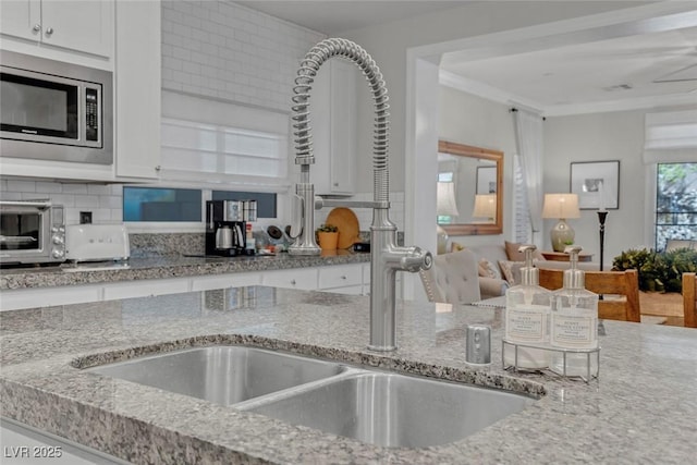 kitchen with a sink, white cabinetry, backsplash, light stone countertops, and stainless steel microwave