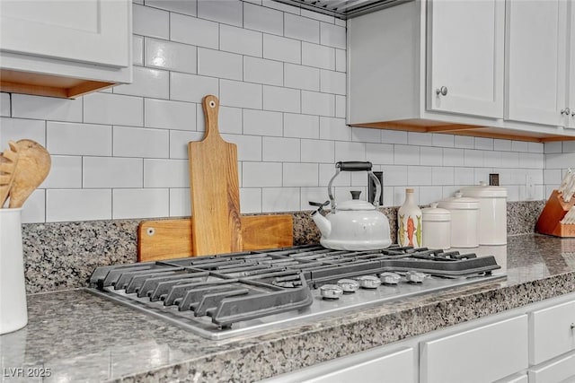 kitchen with light stone counters, white cabinetry, stainless steel gas stovetop, and decorative backsplash