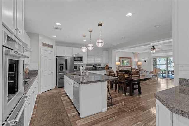 kitchen featuring stainless steel appliances, a sink, visible vents, white cabinets, and backsplash