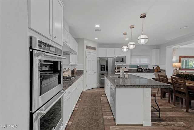 kitchen featuring a breakfast bar area, under cabinet range hood, stainless steel appliances, a sink, and white cabinetry