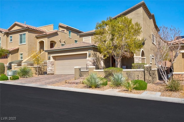 mediterranean / spanish home with an attached garage, fence, stone siding, decorative driveway, and stucco siding