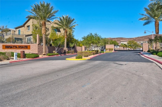 view of street featuring a gated entry, sidewalks, a mountain view, curbs, and a gate