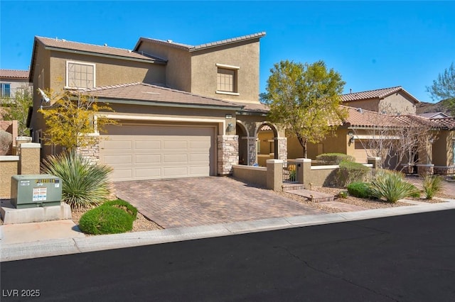 mediterranean / spanish house with a garage, stone siding, decorative driveway, and stucco siding