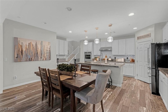 dining room with light wood-type flooring, baseboards, recessed lighting, and stairs