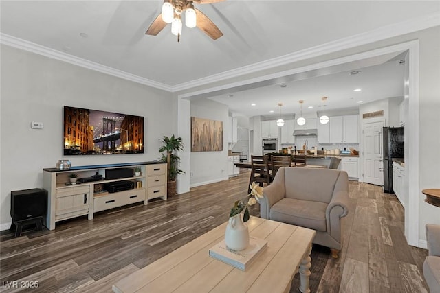 living room featuring wood finished floors, a ceiling fan, baseboards, ornamental molding, and stairway