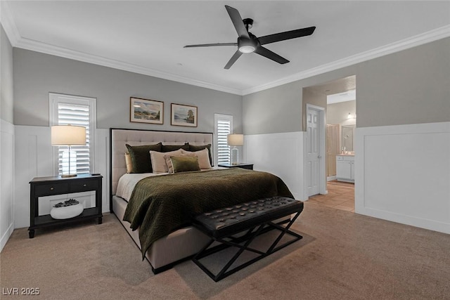 bedroom featuring light carpet, a wainscoted wall, ensuite bath, and ornamental molding