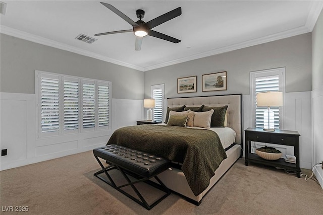 carpeted bedroom featuring ornamental molding, wainscoting, visible vents, and a decorative wall