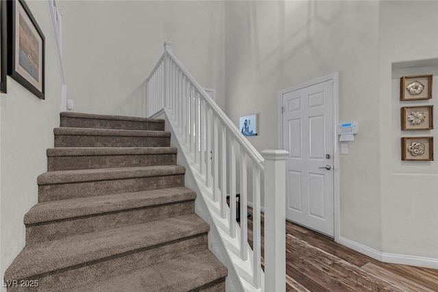 stairway with a high ceiling, wood finished floors, and baseboards