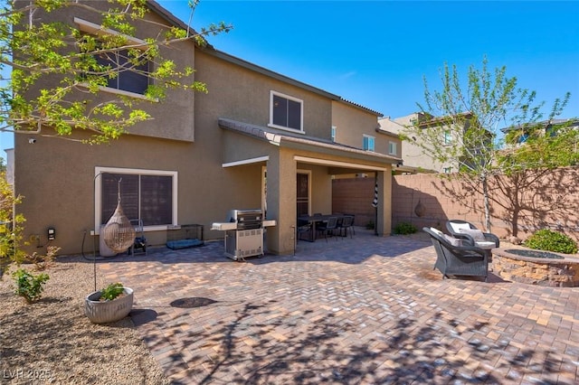 rear view of house featuring a patio, fence, a fire pit, and stucco siding